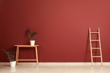 Table with plants and ladder near burgundy wall in big room
