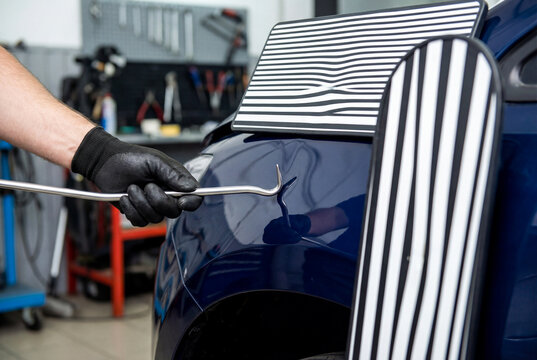 Paintless dent repair PDR technician fixing a dent on a blue car body