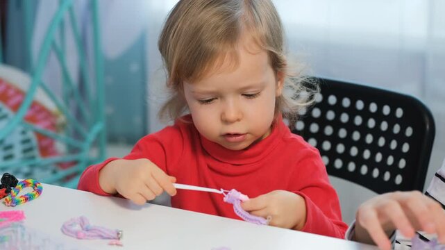 Cute girl and her sister sit at home creating bracelets using colorful rubber bands. They enjoy a fun and creative activity while spending time together