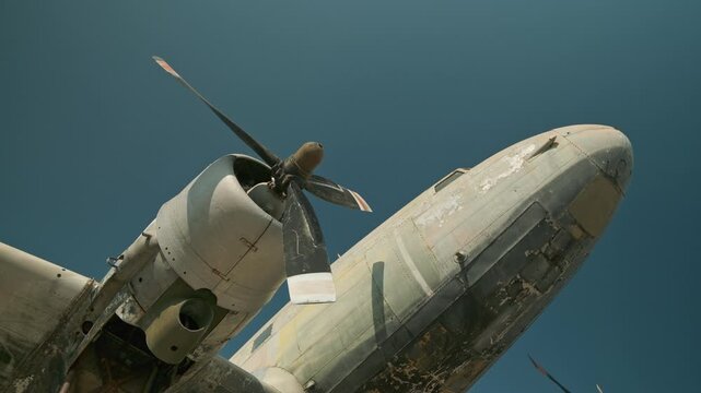 Detailed shot of an old propeller-driven airplane sitting on a runway against a clear blue sky, showing aviation history.