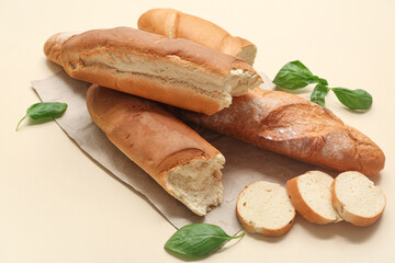 Paper with fresh baguettes and basil on beige background, closeup