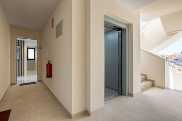 Modern apartment corridor with elevator, staircase and open entrance to residential unit