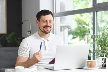 Fototapeta premium Young male teacher with laptop giving online lesson at home