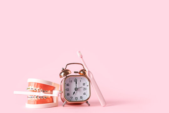 Alarm clock, model of jaw with dental braces and toothbrushes on pink background