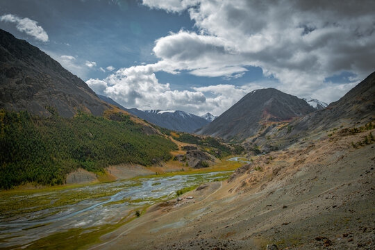  Scenic autumn mountain landscape with a turquoise river valley in the Altai Mountains. Dramatic clouds over rocky peaks.