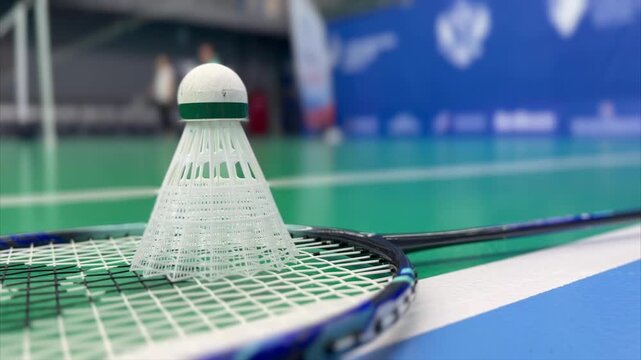 Close-up of a badminton shuttlecock standing on a racket on an indoor court. Shallow depth of field with blurred background creates a dynamic sports training atmosphere