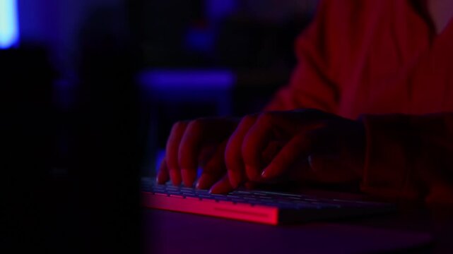 Closeup hand excited senior eldery Asian woman with headphones streamer playing video game using desktop computer at gaming room at home. colorful neon background