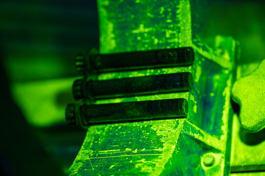 Magnetic particle testing of industrial bolts with bright green fluorescent indication. Non-destructive examination NDT process showing threaded metal fasteners under UV blacklight inspection setup