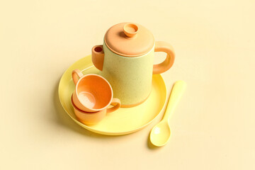 Plate with cups, teapot and spoon for baby on yellow table