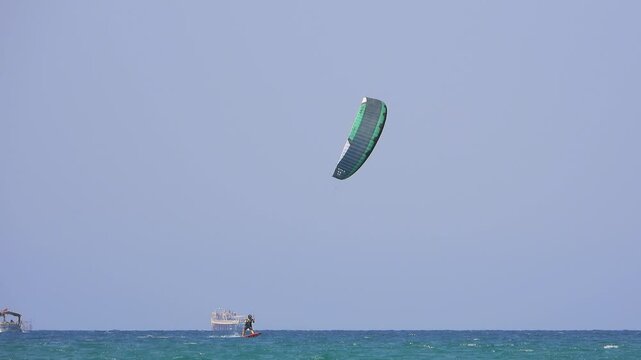 Kiteboarding and kitesurfing as a kiter is pulled across sea water by a power kite. Kiteboarders and kitesurfers ride wind power near the beach for extreme sea sport.