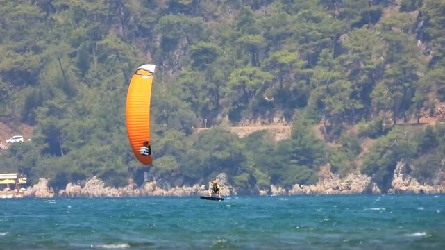 Kiteboarding and kitesurfing as a kiter is pulled across sea water by a power kite. Kiteboarders and kitesurfers ride wind power near the beach for extreme sea sport.