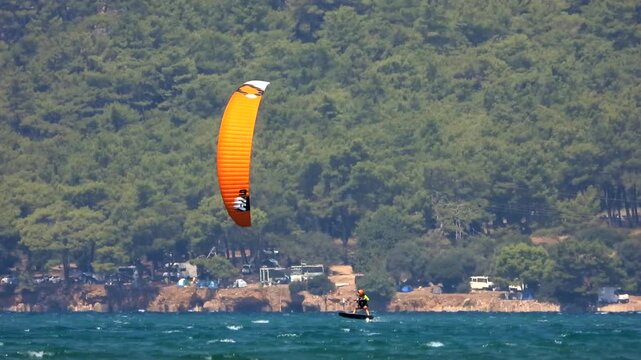Kiteboarding and kitesurfing as a kiter is pulled across sea water by a power kite. Kiteboarders and kitesurfers ride wind power near the beach for extreme sea sport.