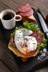 Board with tasty egg Benedict and cup of coffee on wooden background