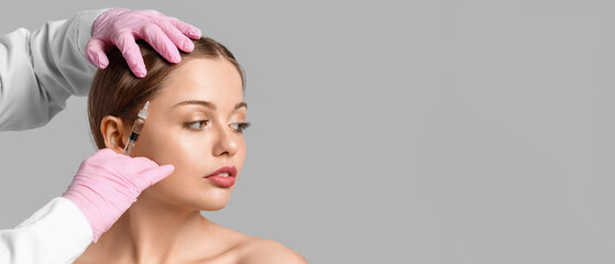 Woman with hair loss problem receiving injection on grey background