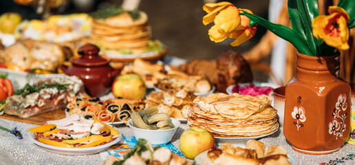Abundant traditional festive table with pancakes, pastries, pies, bread, apples and rustic pottery...