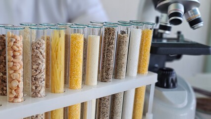 Various grains and pasta placed in test tubes lined up on a shelf next to a microscope in a laboratory setting