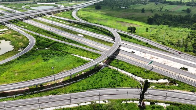 Aerial view of modern highway interchange with multilayer roads and curved ramps surrounded by green farmland, showcasing transportation infrastructure, urban development, and road network planning.