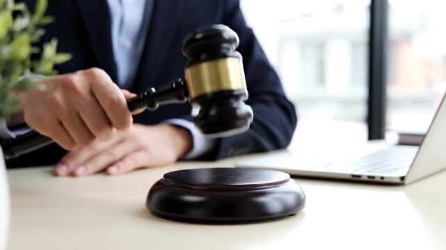 A focused view of a legal professional wielding a gavel over a soundblock with a laptop nearby symbolizing justice and modern legal practice