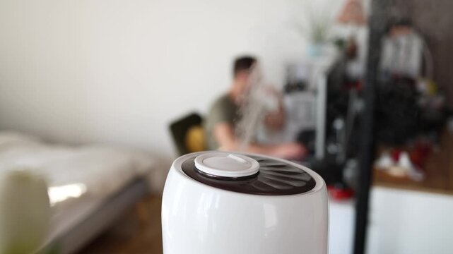 Modern air humidifier device during sitting workplace, young man using computer work on internet, enjoying aromatherapy steam scent from essential oil diffuser in room at home office.