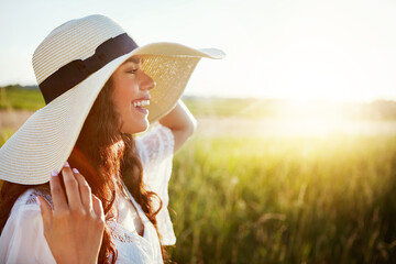 Happy woman, travel and vacation with hat in countryside for summer holiday or outdoor trip. Female person, tourist or smile with lens flare on grass field or space for weekend or fresh air in nature