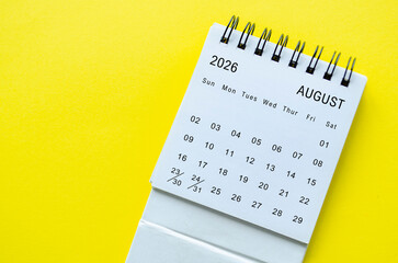 White spiral desk calendar for August 2026 on yellow background with clean composition and space for text.