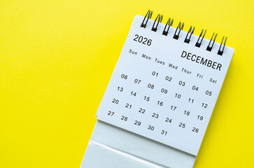 White spiral desk calendar for December 2026 on yellow background with simple design and space for text.