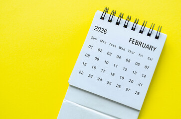 White spiral desk calendar for February 2026 on yellow background with modern style and space for text.
