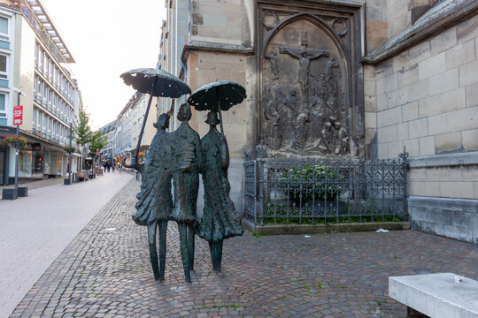 Bronze sculpture of three women with umbrellas in the historic center of Aachen, Germany. Famous landmark near St. Foillan Church in the old town pedestrian zone