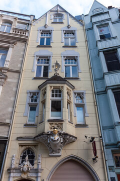 Architectural detail of a historic building facade in Aachen, Germany. Ornate bay window (erker) decorated with a golden knight helmet sculpture and classical decorative elements