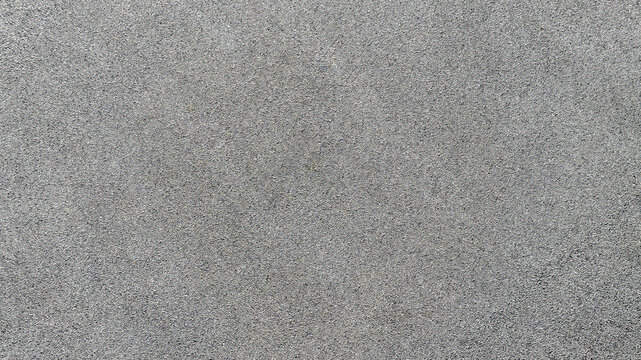 High-angle shot of a dark grey asphalt surface. The fine, grainy texture provides a uniform and neutral background, ideal for urban and industrial design themes, pattern and backgrounds. Zenith view.
