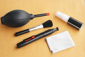 Professional camera and lens cleaning kit on a warm background, including air blower, cleaning pen, soft brush, spray bottle, and microfiber cloth for safe DSLR and mirrorless maintenance.