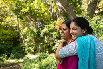 Indian mother and daughter standing in garden hugging in kurtas and jewelry, copy space © wavebreak3