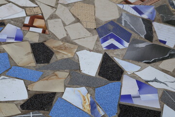 Reused ceramic tile fragments arranged for outdoor flooring, creating an abstract surface with varied colors, irregular patterns, artistic texture, durable design, and visually dynamic composition.
