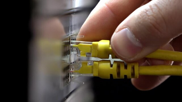 Close-up of a hand plugging an ethernet cable into a network switch in a server rack, data center maintenance and IT connection concept with shallow depth of field.