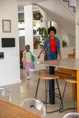 Obraz premium African american mother with daughter entering modern kitchen holding hands by marble island