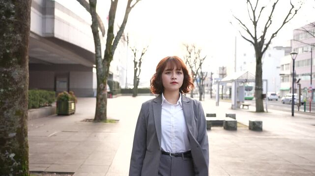 夕方の逆光の中で街を歩くスーツ姿の若い日本人女性