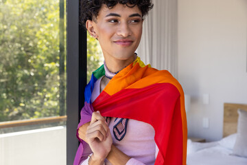 Male standing near door in bedroom draping rainbow pride flag wearing lavender top