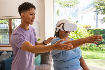 Diverse instructor guiding senior participant using VR headset in living room by sofa, copy space