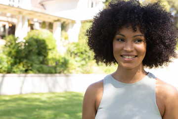 African american woman standing facing right at front backyard with green lawn and shrubs