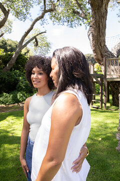 African american mother and daughter standing on backyard lawn under oak trees hugging