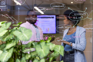 African american coworkers collaborating on marketing plan in office room with glass board