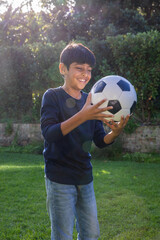 Indian male child smiling with black-and-white soccer ball on sunlit lawn in backyard © wavebreak3