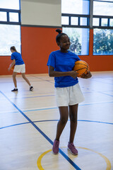 Diverse female teenage teammates practicing basketball in high school gym with basketballs
