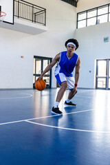 Obraz premium African american male athlete dribbling basketball on court in gym beneath hoop near exit sign