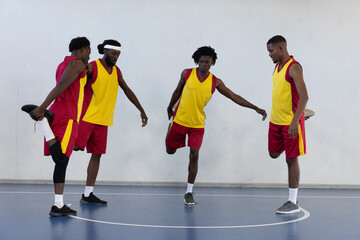 African american male basketball players stretching on blue court by white line in pinnies