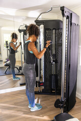 African American woman working out on cable pulley machine in sportswear, mirror reflection in gym