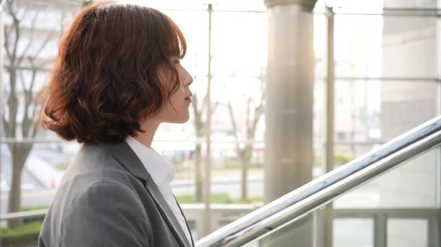 夕方の逆光の中で階段を歩くスーツ姿の若い日本人女性