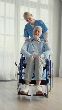 Careful young nurse and old sick man in wheelchair, contemporary nursing home for senior people. Modern healthcare and medicine, caring for elderly, different generations, female health professional