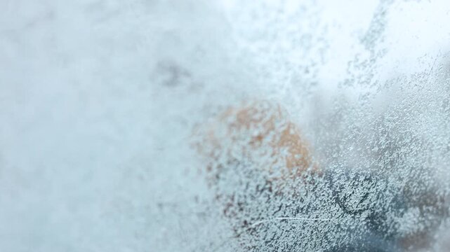 Cinematic daytime scene shown from inside a vehicle, a hand uses a brush to remove packed snow from the front glass. Soft  snow, and cold air.