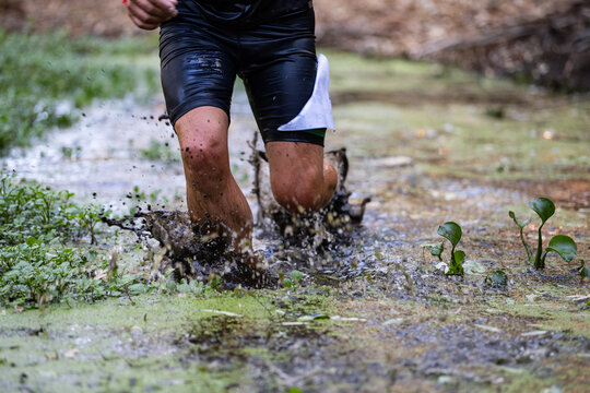 Close-up of a trail runner splashing through muddy water during an off-road race
